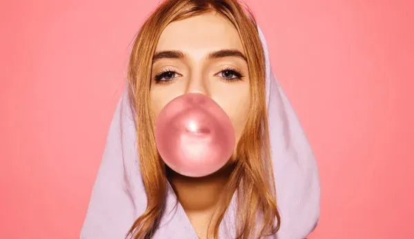 A young woman blowing a vibrant bubble, depicting the stylish experience of chewing HELLO WHATEVER.