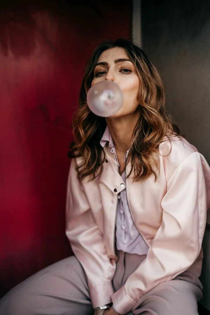A fashion model blowing a bubble while preparing for a backstage runway appearance.